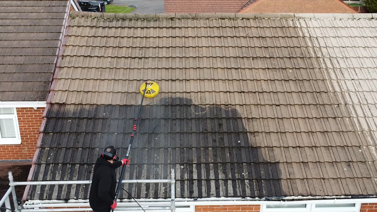 Roof cleaning underway in Kirkby, working from a scaffold tower with the rotary head on a telescopic pole, the washed section showing against the untouched tiles